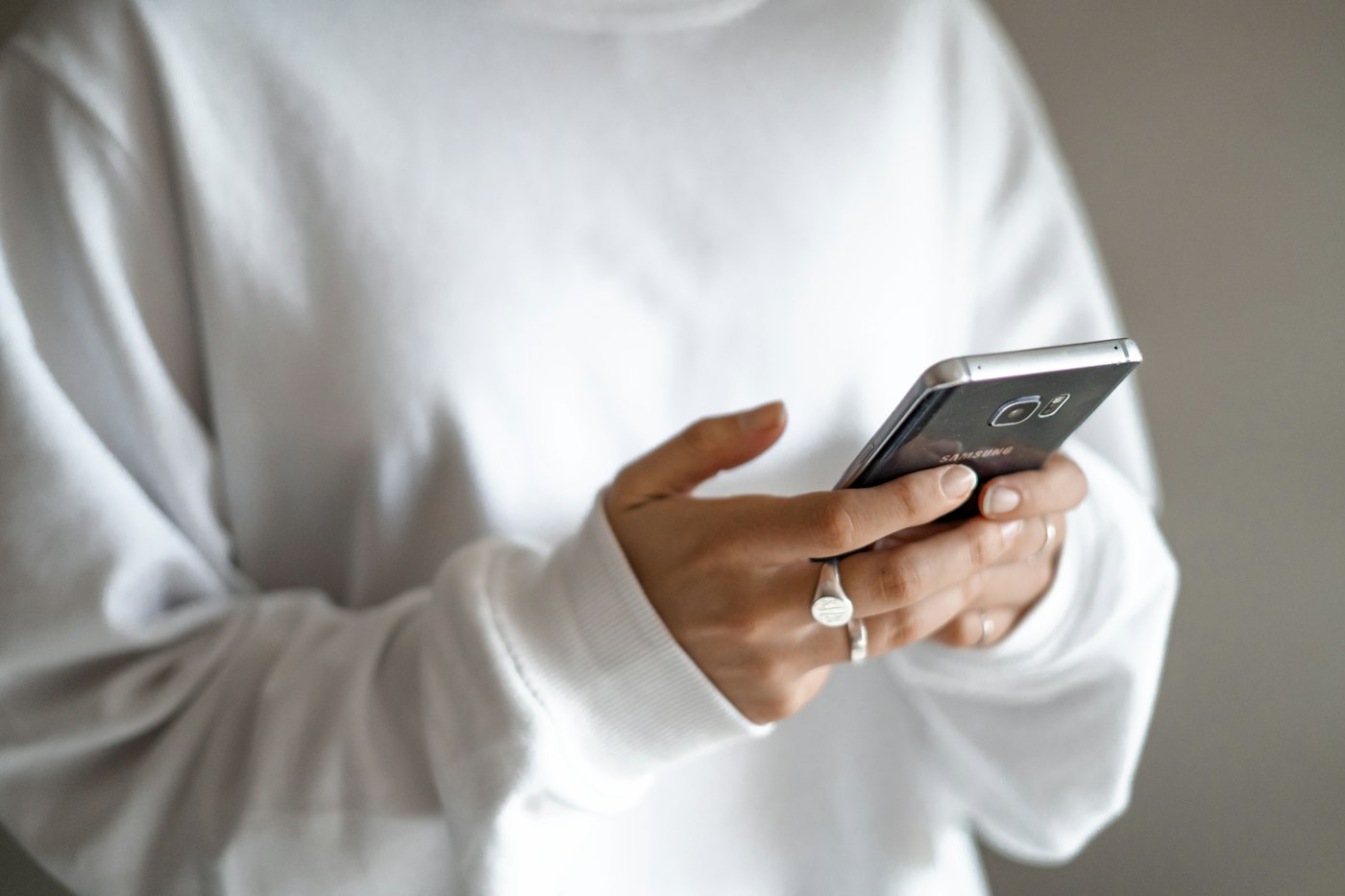 A person in a white sweater typing a text message